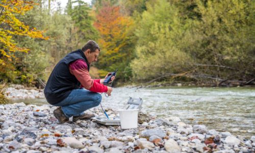 Male biologist using multiparameter instrument while testing dissolved oxygen in river.